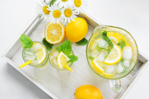 Dos vasos de niebla y un decantador con limonada casera en una bandeja. Bebida refrescante en el caluroso verano. Limones, menta y hielo. Vista superior.