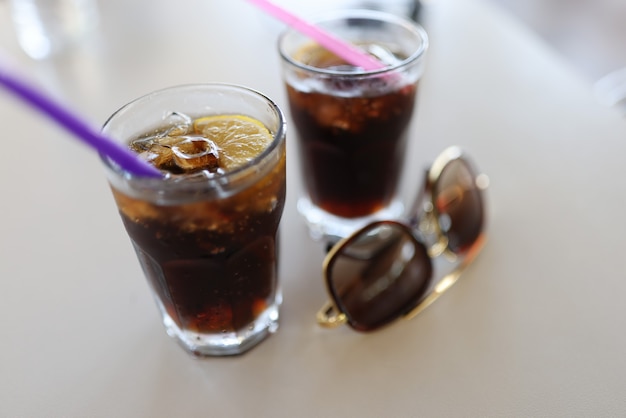 Dos vasos de paja y gafas de sol llenos de pie sobre la mesa blanca