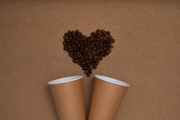 Dos vasos de papel con granos de café en forma de corazón