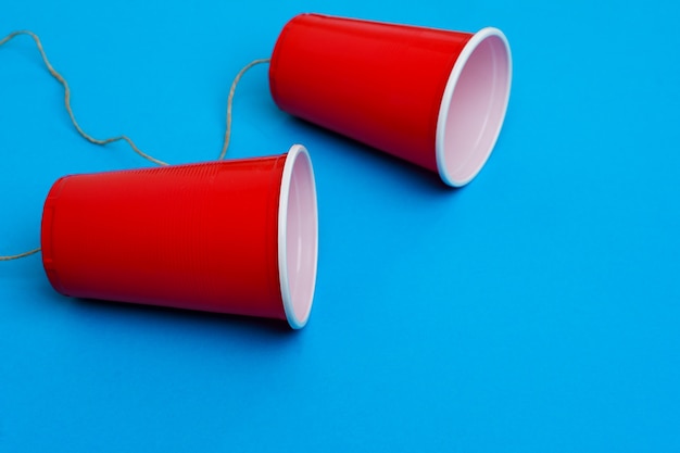 Dos vasos de papel rojo conectados con una cuerda en el teléfono de juguete azul