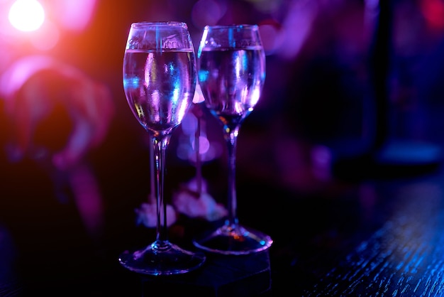 Dos vasos pequeños en una pierna larga sobre una mesa de madera en la luz de la noche con una bebida. Foto de alta calidad
