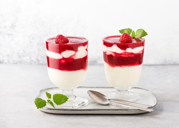 Dos vasos con postre frío en capas Salsa de frambuesa y crema de suero de leche