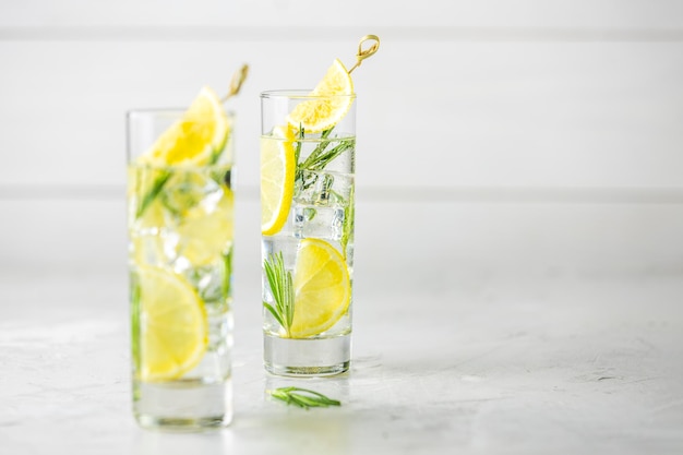 Dos vasos de refrescante bebida de lima limón con cubitos de hielo en copas de vidrio sobre un fondo gris claro Cóctel de refresco de limón fresco de verano con enfoque selectivo de romero