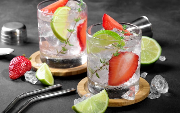 Dos vasos con refresco de fresa de verano o mojito con cubitos de hielo de fresa y lima en la oscuridad