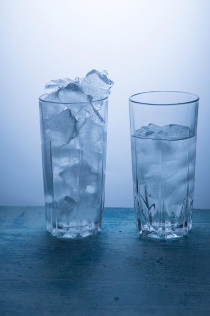 Dos vasos sobre un fondo azul, un vaso lleno de hielo y la otra mitad con agua.