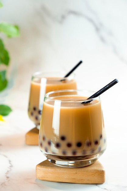 Dos vasos con té de burbujas de leche con deliciosas perlas de tapioca hojas verdes sobre fondo de mármol Famoso té de jalea de leche de Taiwán Bebidas de moda con espacio para copiar