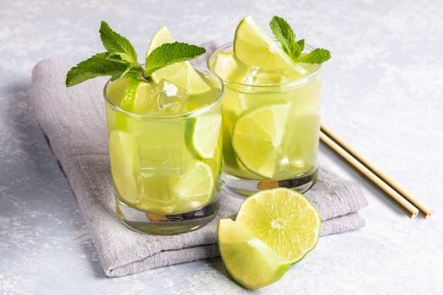 Dos vasos de té verde matcha helado con limón, hielo, menta, pajitas de bambú sobre fondo gris.