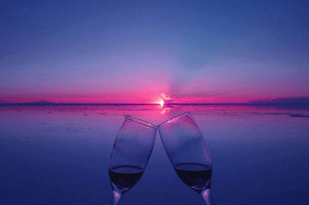 Dos vasos tintinean para celebrar al atardecer sobre inundaciones de salinas, Uyuni, Bolivia