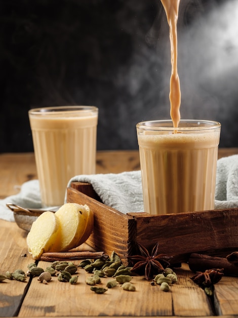 Dos vasos de vidrio facetado sobre una mesa de madera con la tradicional bebida india masala chai.