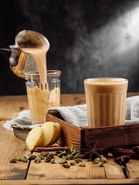 Dos vasos de vidrio facetado sobre una mesa de madera con la tradicional bebida india masala chai.