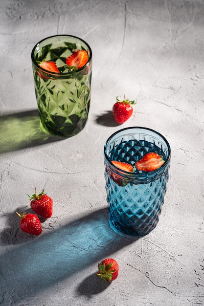 Dos vasos de vidrio geométrico verde y azul con agua fresca y frutas de fresa