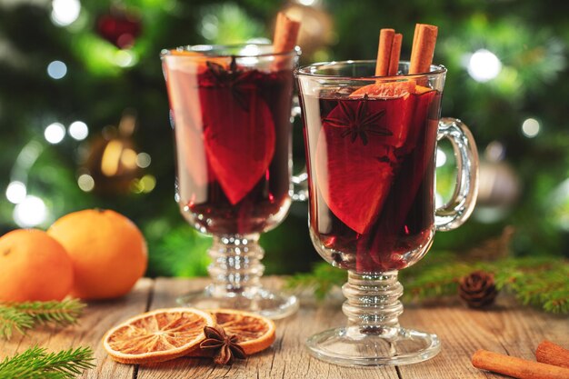 Dos vasos de vino caliente de Navidad o gluhwein con especias y rebanadas de naranja en una mesa rústica contra el árbol de Navidad Bebida tradicional en las vacaciones de invierno