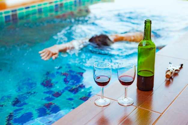 Dos vasos de vino tinto cerca de la piscina con un hombre está nadando en la piscina