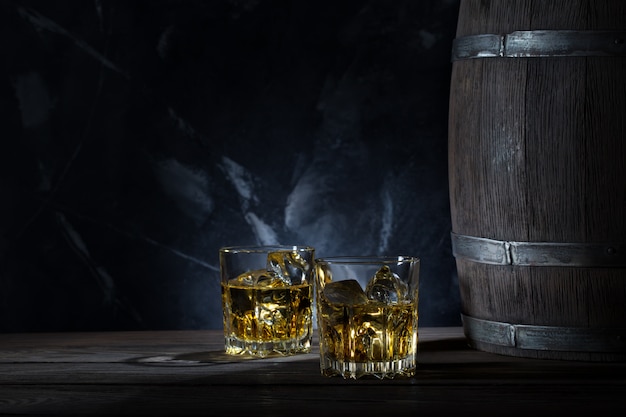 Dos vasos de whisky con hielo y barril de madera.