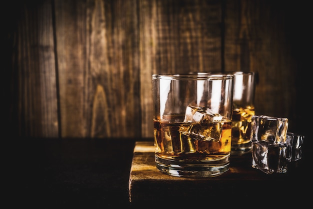 Dos vasos de whisky en la mesa de madera oscura, con cubitos de hielo,