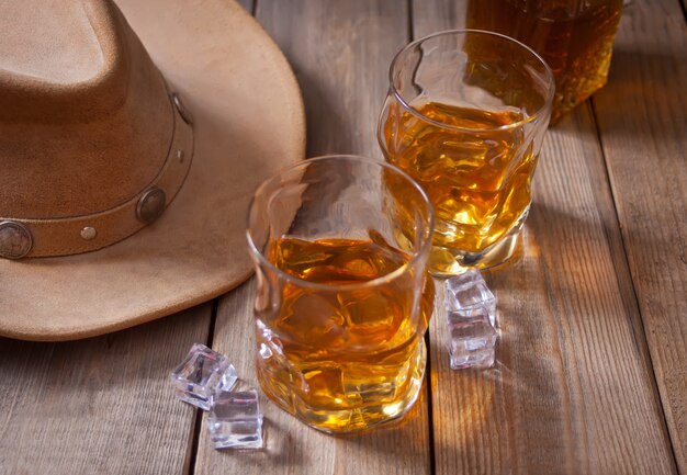 Dos vasos de whisky y sombrero de vaquero en la mesa de madera.