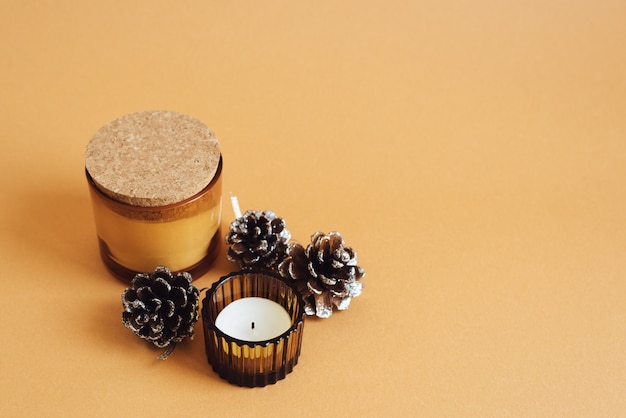 Dos velas aromáticas y piñas decorativas sobre fondo naranja