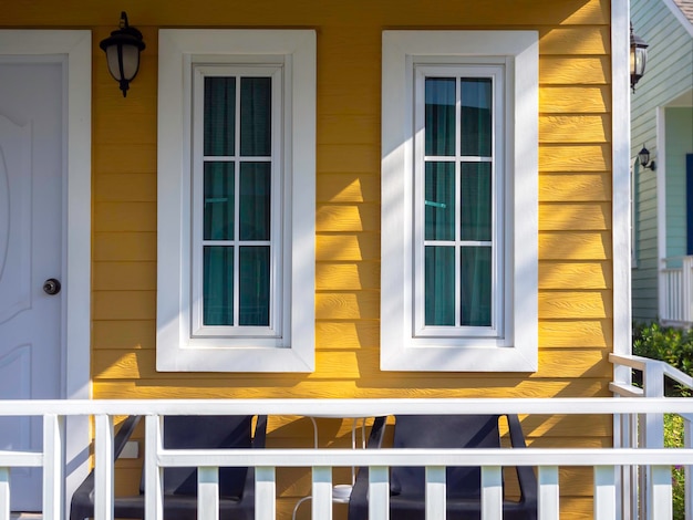 Dos ventanas de la casa blanca con vidrio, decoración de cortinas verdes en el residente de madera amarilla cerca de la puerta principal y la terraza, vista desde el exterior.