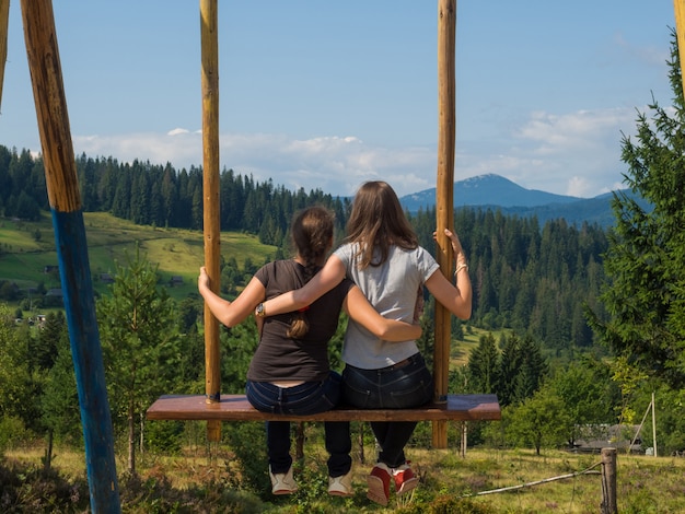 Dos viajeros disfrutan de balancearse en un columpio celestial y vistas a la montaña