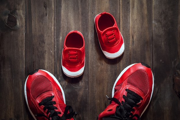 Dos zapatos deportivos rojos o zapatillas de deporte de madre o padre y niño sobre fondo de madera