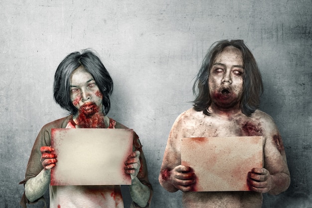 Foto dos zombies de miedo con sangre y heridas en su cuerpo sosteniendo un letrero