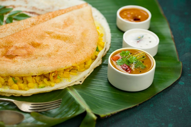 Dosa Masala dosaberühmter südindischer Frühstücksartikel, der auf traditionelle Weise in einer Gusseisenpfanne hergestellt und auf einem frischen Bananenblatt mit dunkelgrünem Hintergrund isoliert wird