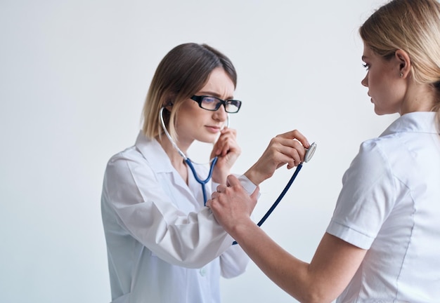 Doutor de roupa médica com um estetoscópio examina um paciente em um fundo claro Foto de alta qualidade