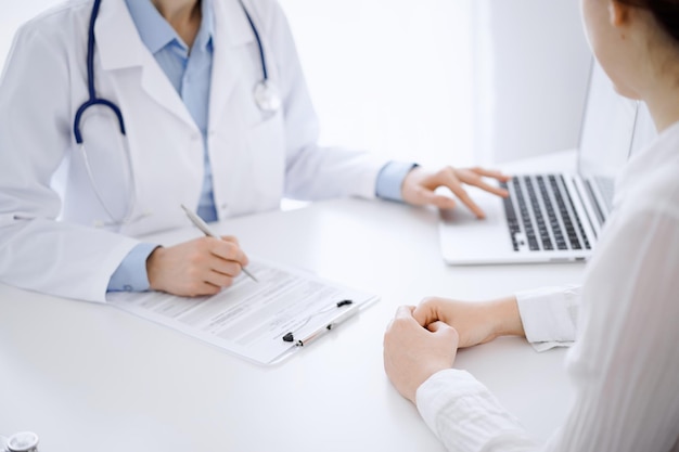 Doutor e paciente discutindo algo e usando laptop enquanto estão sentados um em frente ao outro na mesa no escritório da clínica. Conceito de serviço médico e medicina perfeito