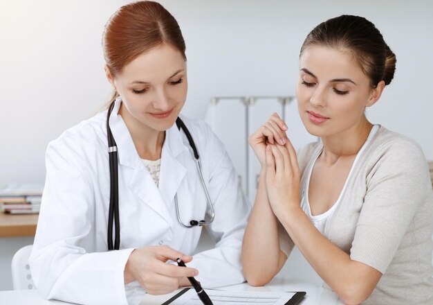 Foto doutor e paciente sentados e discutindo os resultados do exame de saúde na clínica ensolarada.