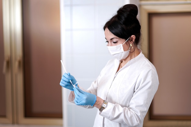 Doutor em uma máscara médica. Tomando um cotonete da orofaringe. Fotografia conceitual - teste de coronavírus. Na mão é um tubo de ensaio com uma amostra do paciente.
