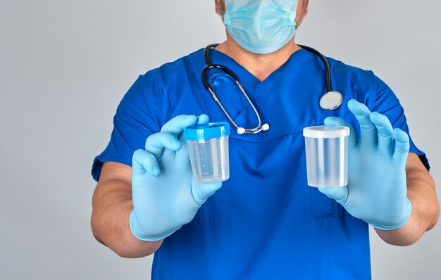 Doutor em uniforme azul e luvas de látex está segurando um recipiente de plástico vazio para tirar amostras de urina