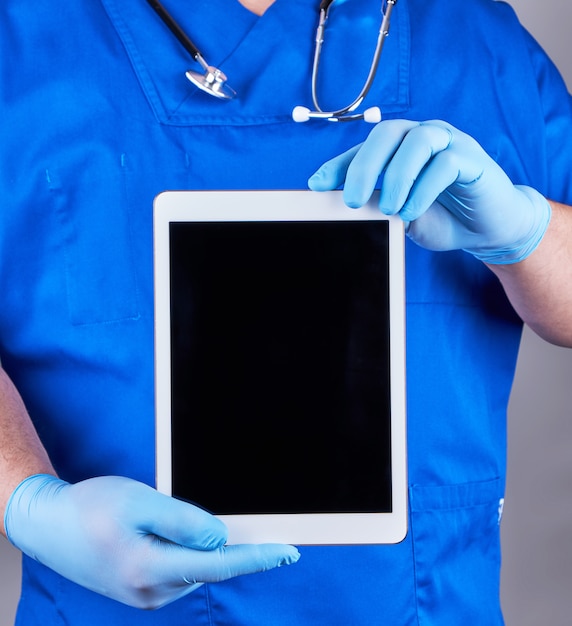 Doutor em uniforme azul e luvas estéreis de látex segurando um tablet eletrônico com uma tela preta em branco