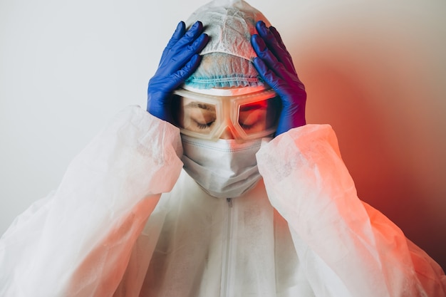 Foto doutor em uniforme de proteção, óculos, luvas, sobre um fundo azul na luz de neon. retrato de close-up de um médico em néon vermelho. homem cansado está lutando contra um coronavírus. covid 19