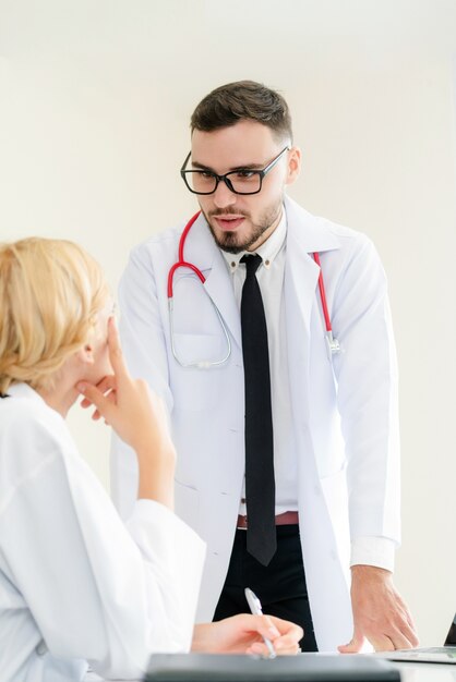 Foto doutor fêmea novo no hospital que tem a conversação com um outro doutor que está ao lado da tabela.