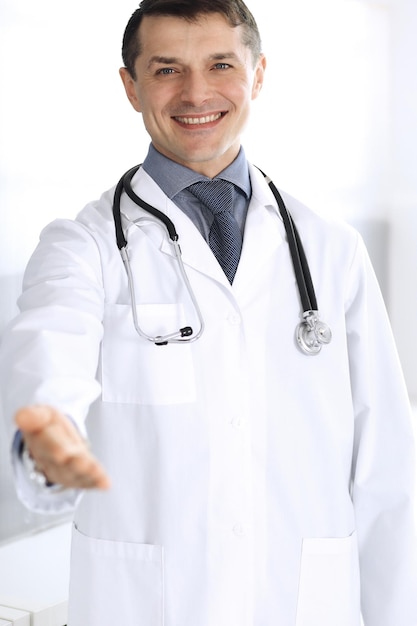 Doutor homem alegre sorrindo para a câmera, ajudando a mão. Serviço médico perfeito na clínica. Futuro feliz em medicina e saúde.