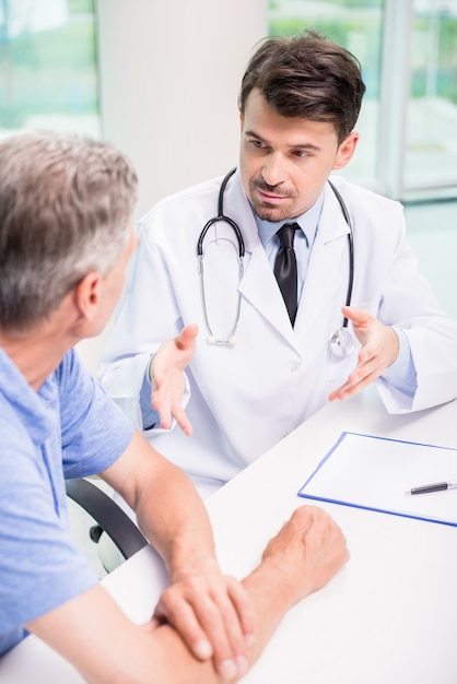 Doutor masculino que fala com o paciente seriamente na clínica.