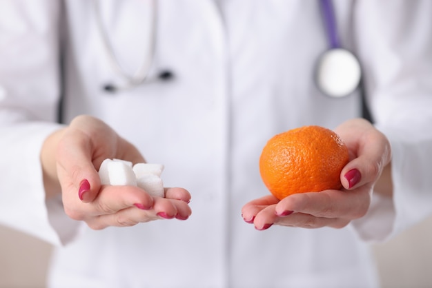 Doutor, segurando cubos de laranja e açúcar em suas mãos closeup. Conceito de prevenção do diabetes