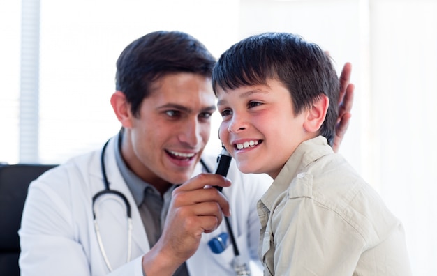 Doutor sorridente que examina os ouvidos do menino