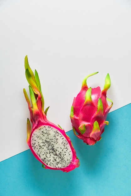 Dragonfruit orgánico fresco (pitaya o pitahaya) cortado por la mitad en dos tonos de menta azul dividida y pared blanca. Diseño plano creativo con frutas exóticas de moda en vibrantes colores rosa y verde.