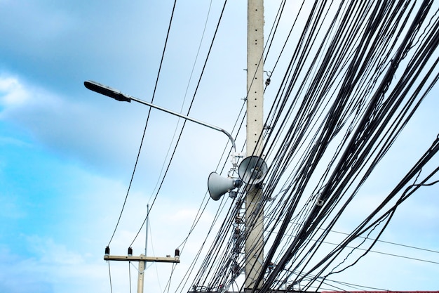 Draht, Leuchtstofflampe und Lautsprecher auf elektrischem Pfosten in Thailand mit blauem Himmel.