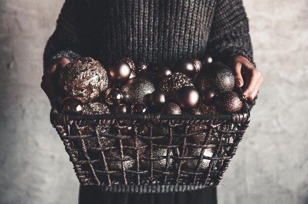 Drahtkorb voller Weihnachts- oder Neujahrsbaum goldener Vintage-Dekorationsspielzeug in den Händen einer Dame in einem grauen warmen Pullover, selektiver Fokus, quadratische Ernte