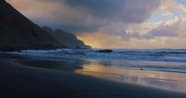 Dramático amanecer en el mar Cielo ardiente y brillantes olas doradas Hermosa playa con arena negra y olas suaves perfectas para relajarse y nadar