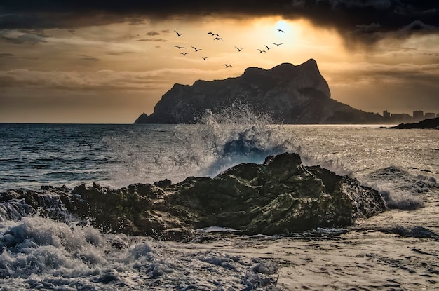 Dramático paisaje marino al atardecer de una ola salpicando en una roca