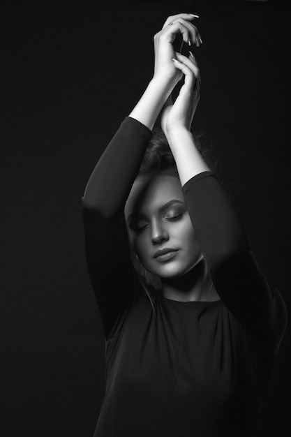 Dramático retrato de una mujer joven sensual posando en una habitación oscura con los ojos cerrados. Retrato en blanco y negro