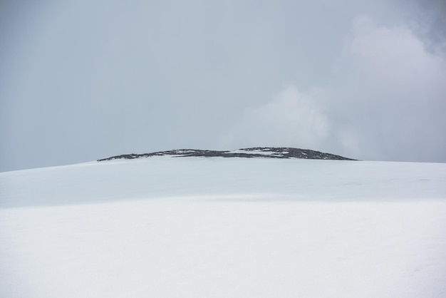 Dramatische Alpenlandschaft mit riesiger schneebedeckter Bergkuppel mit felsiger Spitze im Sonnenlicht unter grauem bewölktem Himmel Ehrfürchtige Berglandschaft mit hohem Schneeberg in Kuppelform in der Mitte bei wechselhaftem Wetter
