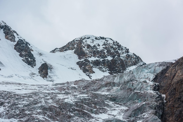 Foto dramatische landschaft mit großen eisfällen auf gletschern unter schnee bergspitzen im grauen bewölkten himmel scharfe felsen und wunderschöne gletscher mit eisfällen in großer höhe trostlose landschaft in bergen in bewölkter luft