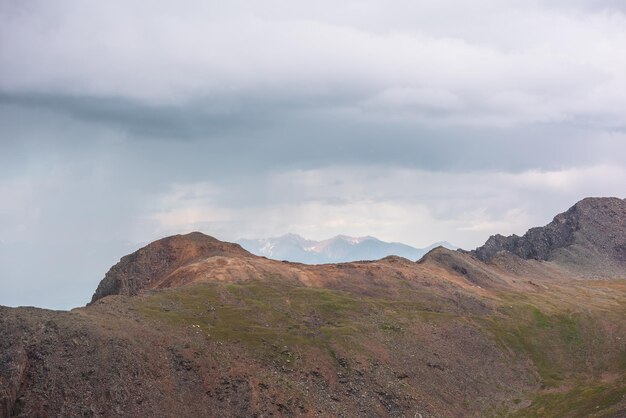 Dramatische Luftlandschaft mit sonnenbeschienenem Berggipfel bei Regen bei wechselhaftem Wetter Atmosphärische Berglandschaft mit scharfen Felsen im Sonnenlicht unter bleigrauem bewölktem Himmel Regenwolken in den Bergen