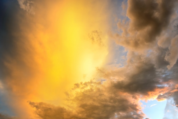 Dramatische Sonnenuntergangshimmellandschaft mit geschwollenen Wolken, die von orange untergehender Sonne und blauem Himmel beleuchtet werden.