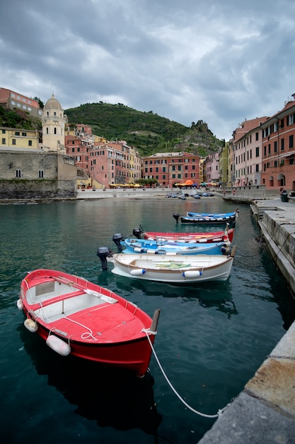 Dramatischer bewölkter Himmel über dem Hafen von Vernazza, mit einigen Booten im Vordergrund. Cinque Terre, Italien.