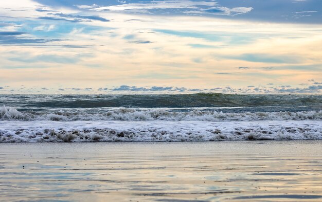 Dramatischer bewölkter Himmel vor dem Abend am Meeresstrand mit Himmelsreflexion und Wellen